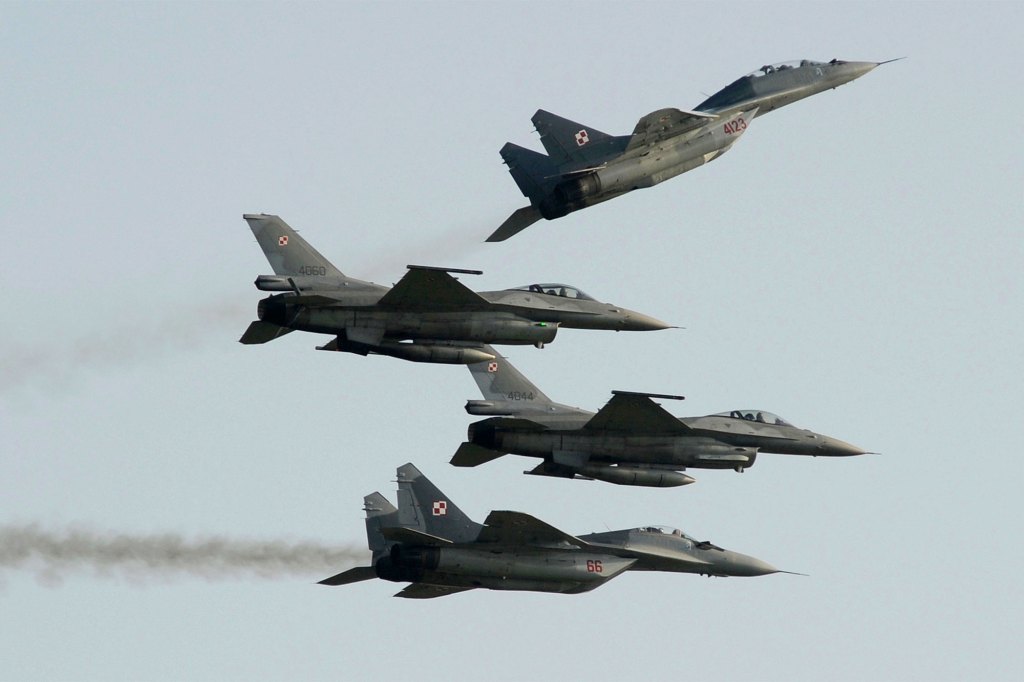 Dos aviones de la Fuerza Aérea Polaca Rusa vuelan un MiG-29 por encima y por debajo de dos aviones de la Fuerza Aérea Polaco-Estadounidense construidos aviones de combate F-16 durante la exhibición aérea en Radom, Polonia, el 27 de agosto de 2011.